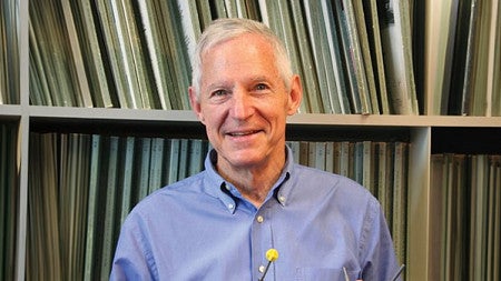 a headshot of John E. Baldwin, posed in front of a bookcase of folders