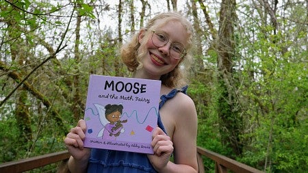 a student holds her book with a background of trees