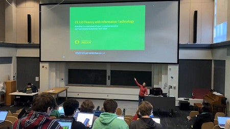 inside a classroom, a person points to a powerpoint slide