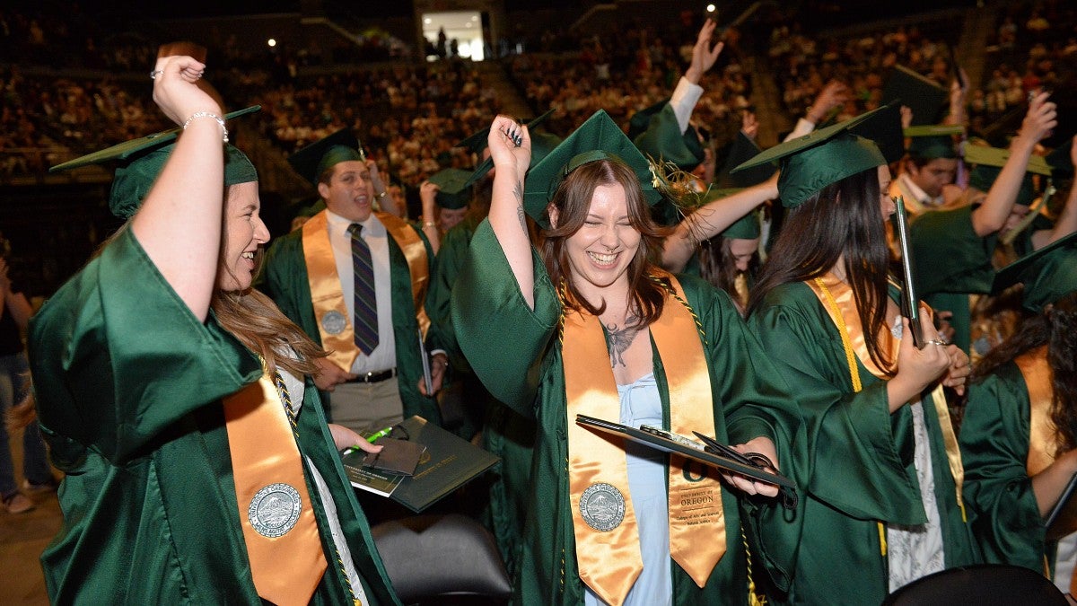 Students in their green robes cheer at the Spring 2024 Commencement