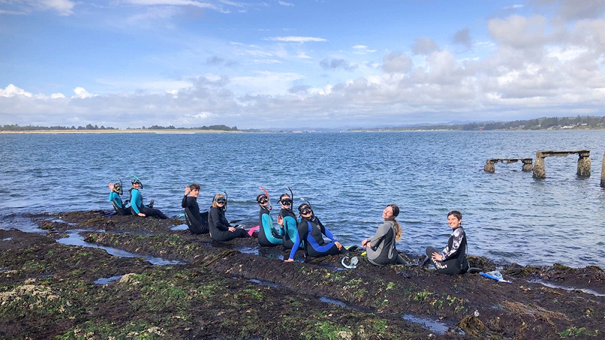 Group of marine biology students posing for group photo on a rocky beach