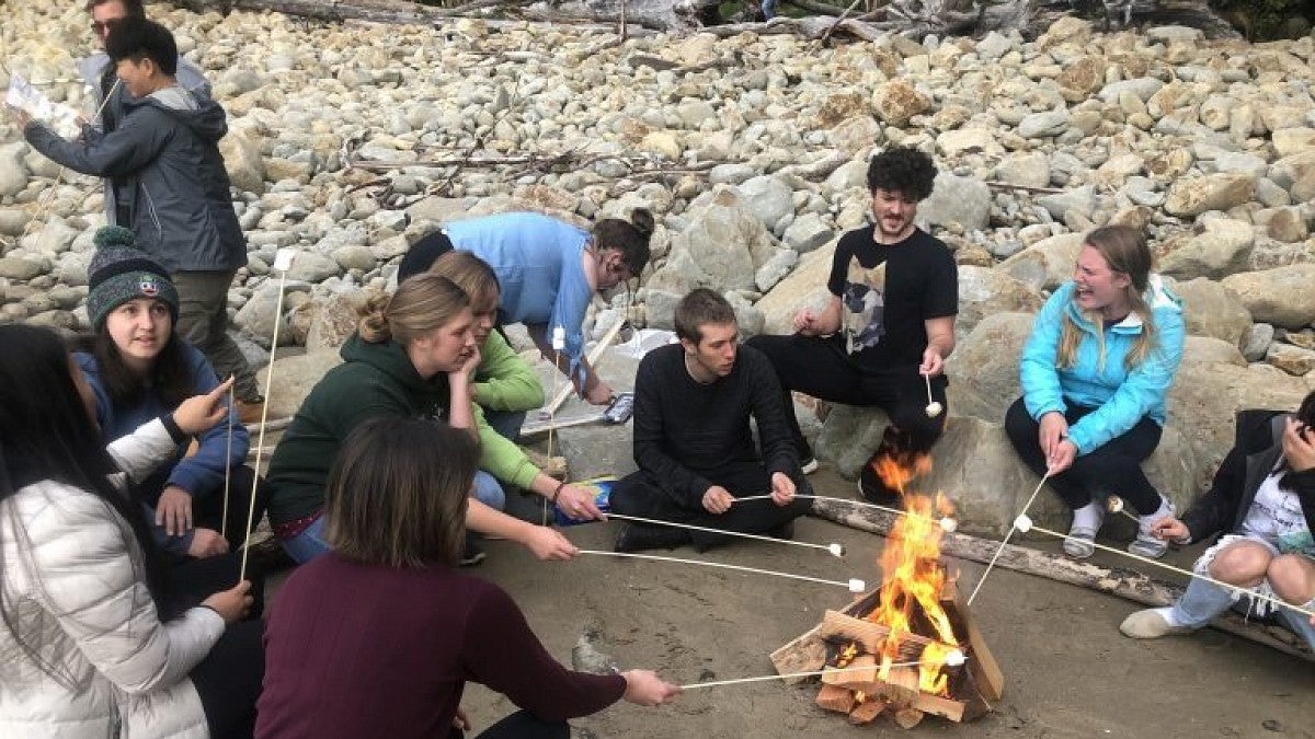 OSMA students sitting on a beach roasting marshmallows