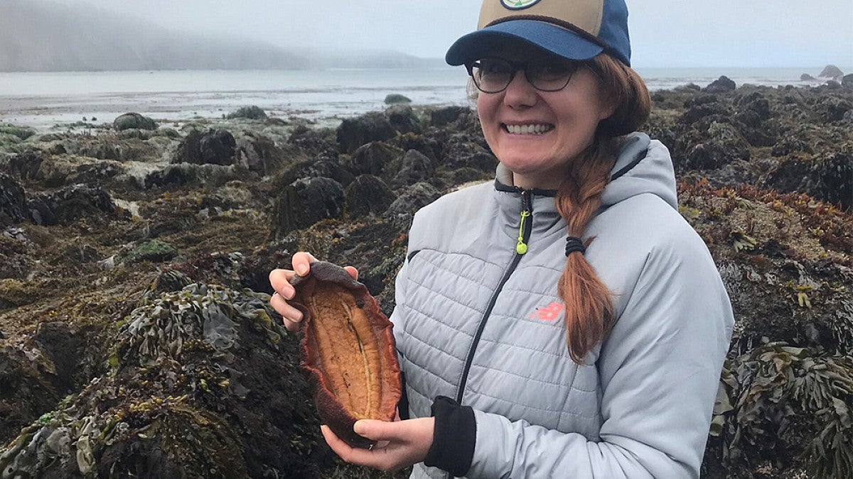 Research student holding a shell standing on Oregon coast