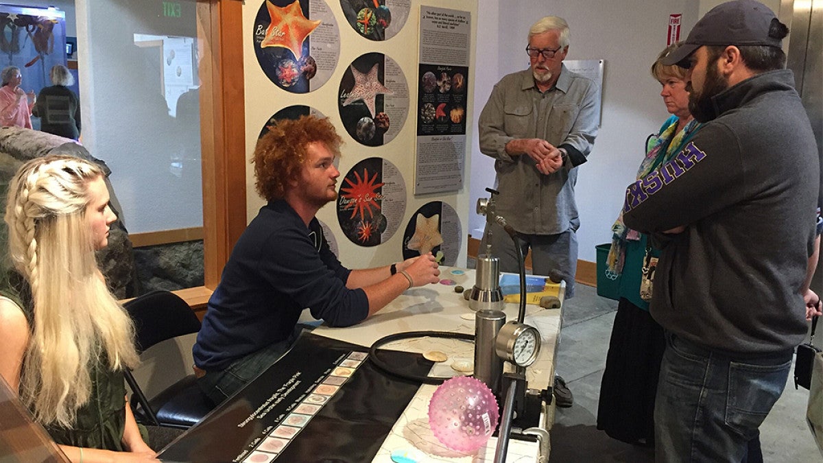 Students sitting at table explaining marine biology equipment 