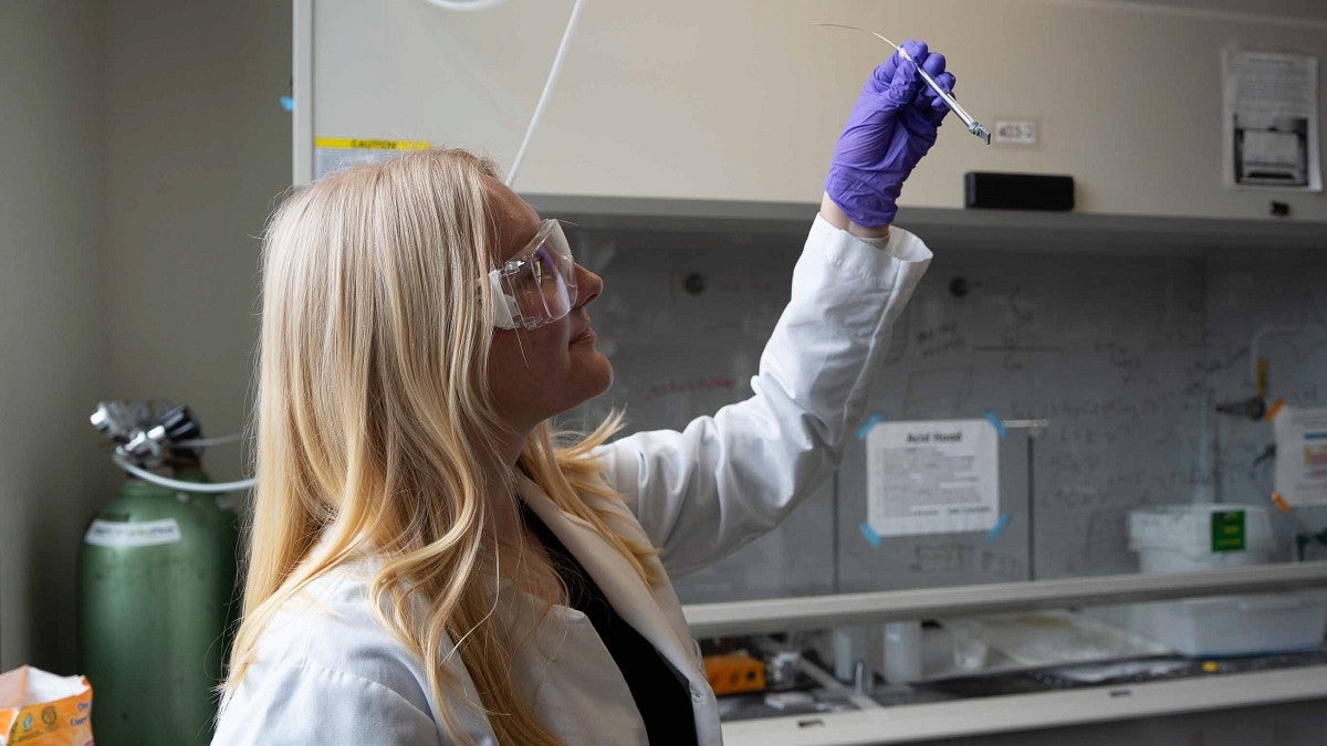 Woman in lab coat holding up a tube