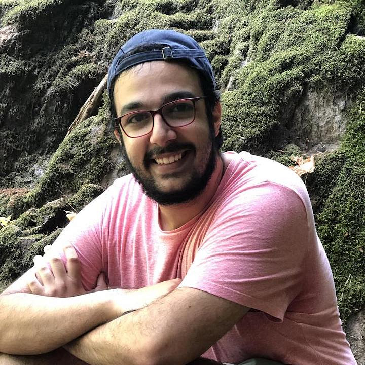 biology alum ryan sayegh sitting in front of moss-covered rock outcropping