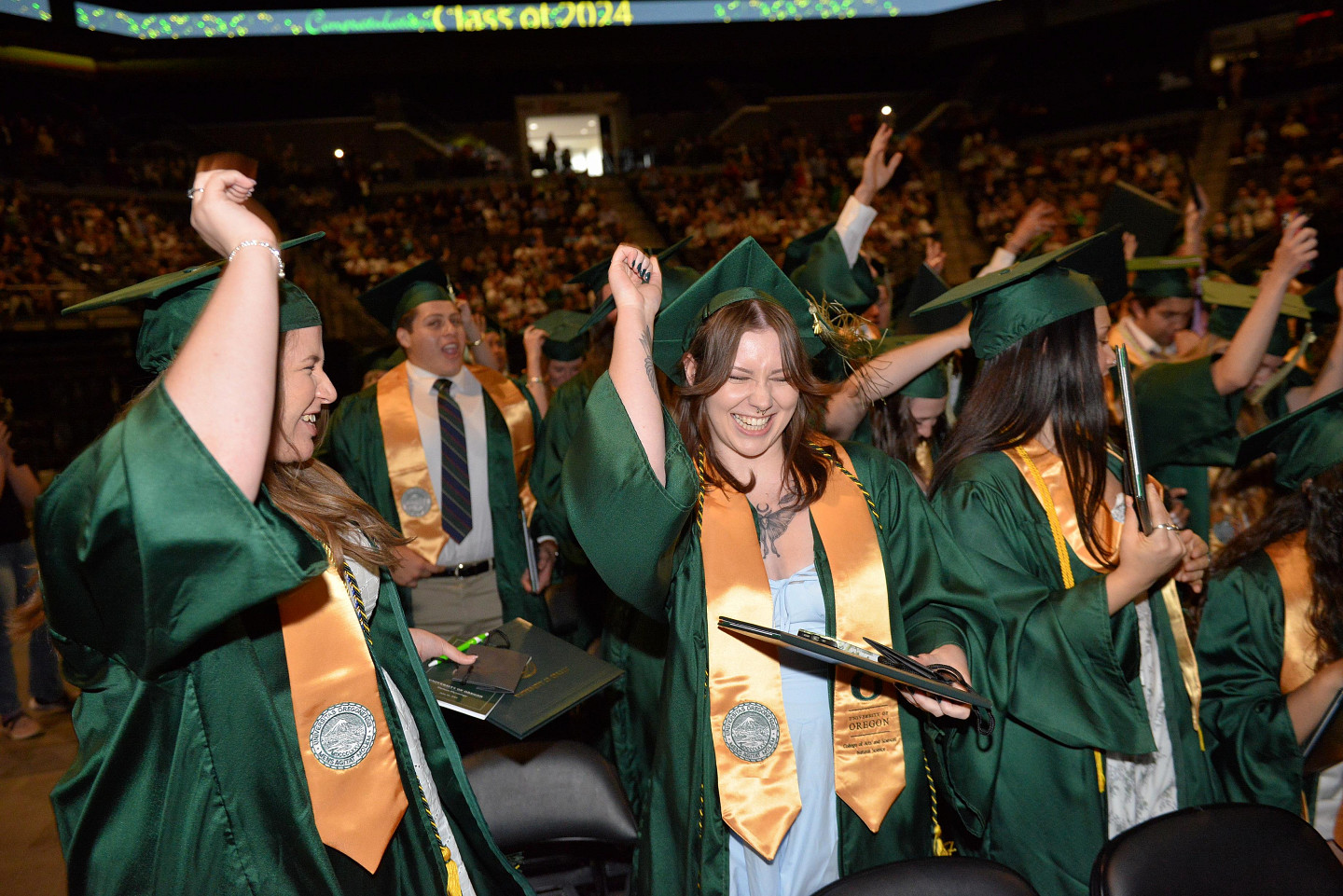 Students in their green robes cheer at the Spring 2024 Commencement