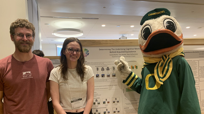 Psychololgy students standing next to a research poster with the Duck mascot